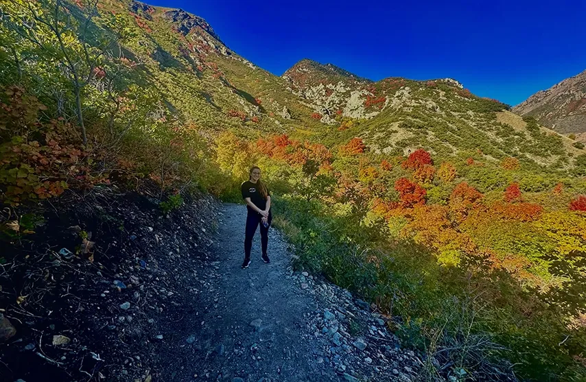 Cristina Lugo stands on a dirt path surrounded by yellow and red trees.